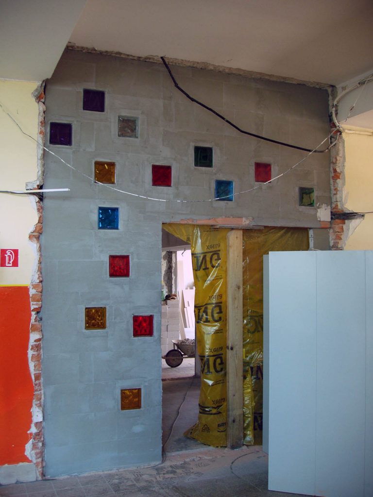 Vymurovanie steny oddeľujúcej priestor kaplnky/knižnice od školského priestoru. Pôvodná presklenná stena sa demontovala a ako odkaz na svetlo a charakter priestoru, ktorý sa ukrýva za stenou, boli použité sklenené tvárnice. Umiestnenie tvárnic je abstraktným zobrazením letu holuba - evokuje zasvätenie kaplnky Duchu Svätému.